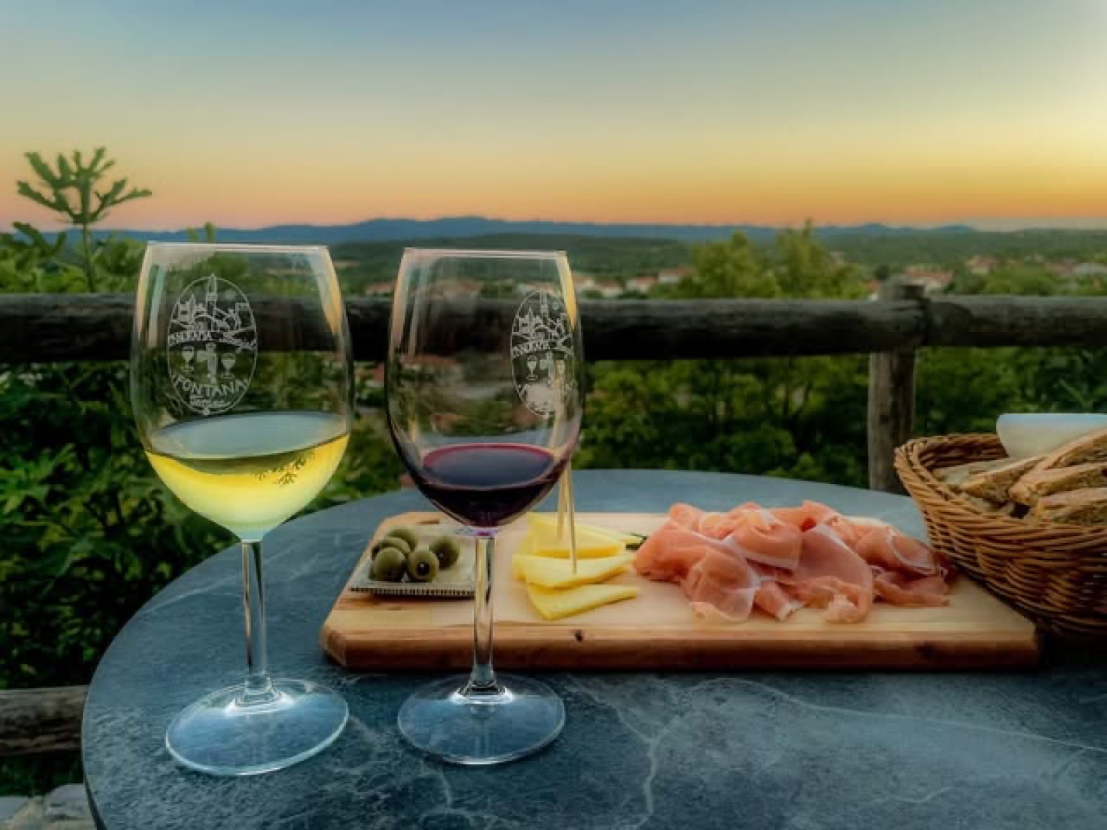 Kozarca vina Fontana terana in pršut na terasi ob sončnem zahodu